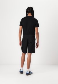T-shirt noir à manches courtes et short cargo noir avec poches. Porté avec des chaussures de sport bleues et des chaussettes blanches. Design simple et décontracté.