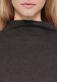 Σκοτεινό γκρι πλεκτό μπλουζάκι με ψηλό, διπλωμένο γιακά και υφή υφάσματος. Το ρούχο παρουσιάζει μία λεία επιφάνεια με ένα λεπτό, ομοιόμορφο πλέγμα.