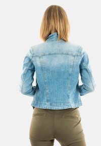 Ljusblå denimjacka med en figursydd silhuett, knäppta manschetter och en klassisk krage. Slät textur, synliga sömnadsdetaljer och ryggklädd.