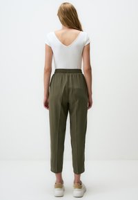 Body blanc à côtes avec dos en V, associé à un pantalon vert olive, fuselé, avec une ceinture élastique et une longueur cheville. Baskets blanches.