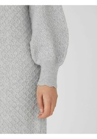 Ljusgrå tröja med en texturerad diamantmönster, ribbade ärmslut och vågformad nederkant på ärmarna. Mjuk stickad tyg.