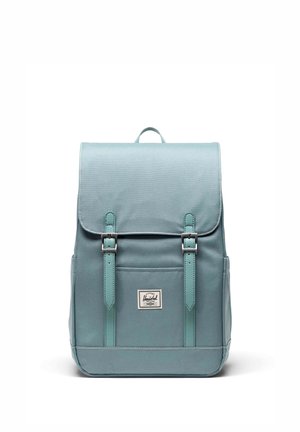 Tyrkysový batoh z látky má klopu so zapínaním na dve nastaviteľné remene, predné vrecko a značkovú nášivku. Hladká textúra so šitými akcentmi.