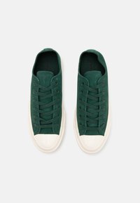 Baskets basses en daim vert avec bout rond, semelle en caoutchouc blanche et œillets métalliques pour les lacets. Texture lisse et embout en caoutchouc contrastant.
