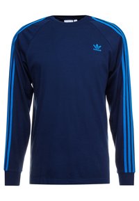 Sudadera de manga larga en color marino con diseño de tres rayas azules en los hombros, puños acanalados y un logo de Adidas bordado en azul en el pecho.