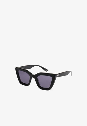 Zwarte oversized zonnebril met cat-eye vorm, donkere glazen en een klein wit logo op het pootje.