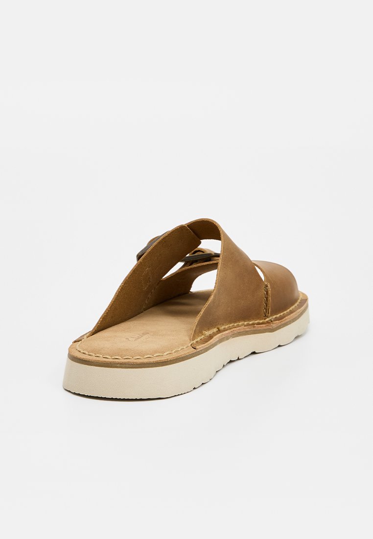 Sandale en cuir brun avec des côtés ouverts, une semelle plate et une semelle extérieure beige cousue pour une meilleure traction et durabilité.