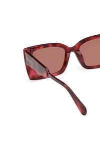 Ochelari de soare roșii, de formă rectangulară, cu un model translucid, lentile maro și brațe din plastic elegante, având detalii de brand gravate.