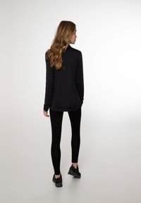Top nero a maniche lunghe abbinato a leggins neri e scarpe sportive nere. Tessuto liscio e design aderente, visto da dietro.