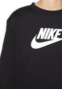 Felpa nera a maniche lunghe in cotone con un grande logo Nike bianco sul petto. Collo rotondo con una texture morbida.