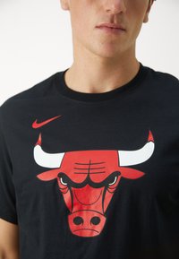 Black cotton t-shirt featuring a large red and white bull logo on the front, sleek crew neckline, and short sleeves.