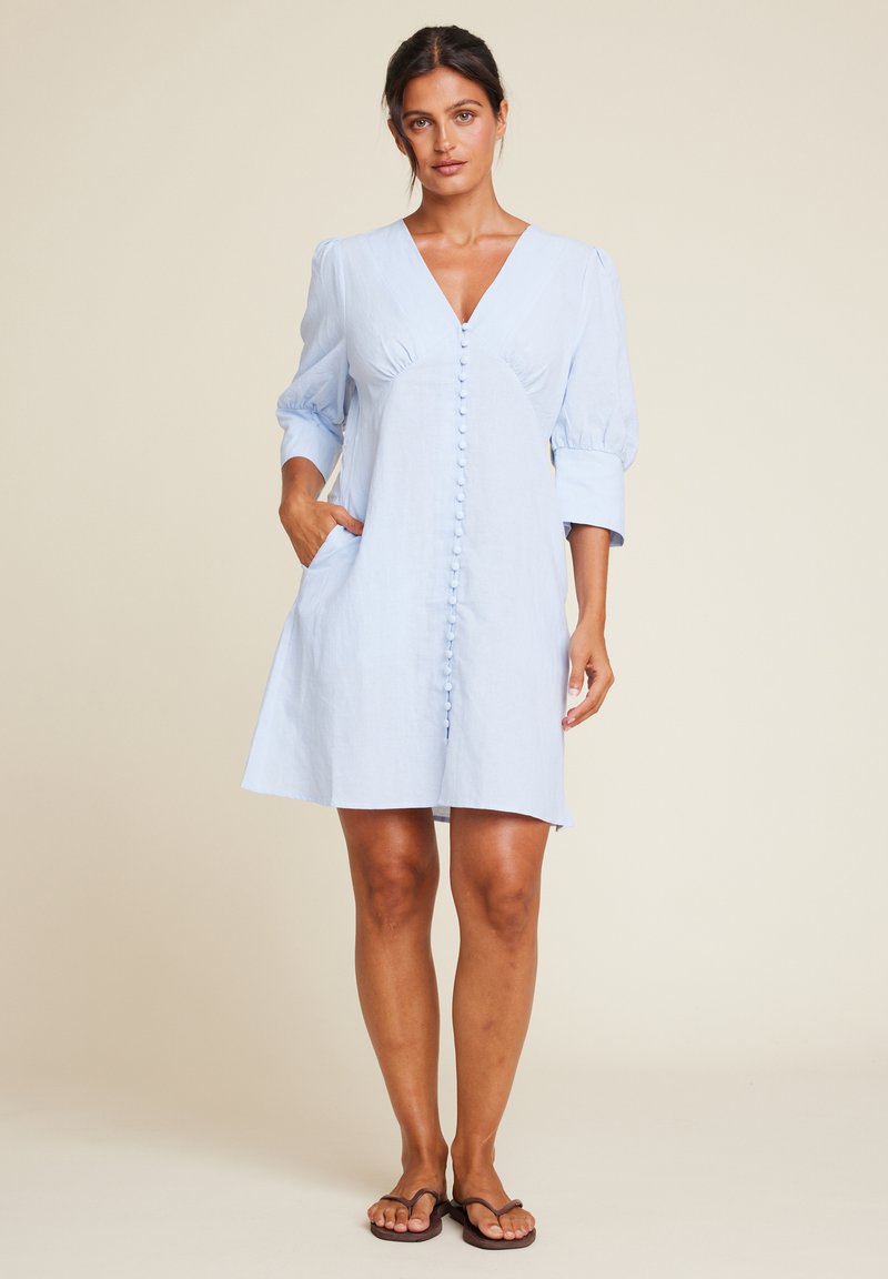 Lyseblå kort kjole med V-hals, puffede ærmer og knaplukning foran, med sidelommer og en afslappet pasform.