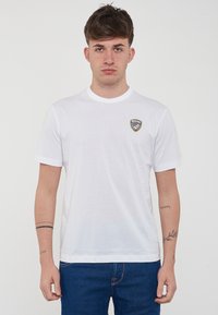T-shirt bianco in cotone con maniche corte, colletto tondo e piccolo logo a scudo ricamato sulla parte sinistra del petto. Tessuto semplice e vestibilità casual.