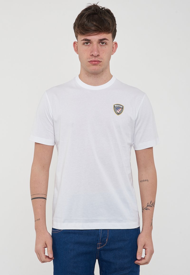 T-shirt bianco in cotone con maniche corte, colletto tondo e piccolo logo a scudo ricamato sulla parte sinistra del petto. Tessuto semplice e vestibilità casual.