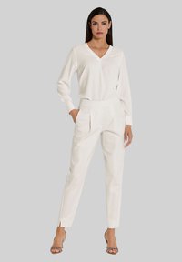 Weißes Langarmshirt mit V-Ausschnitt, kombiniert mit weißen plissierten Hosen und Riemchensandalen. Glatte Textur mit enganliegenden Silhouette.