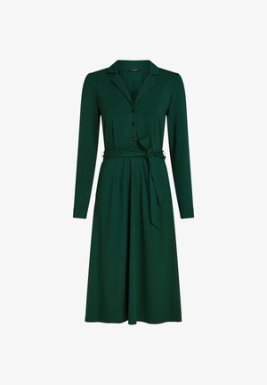 Abito verde con maniche lunghe, colletto e chiusura a bottoni. Presenta un girovita annodato e piccole pois neri su un tessuto liscio.