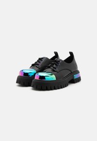 Sapatos de pele preta com uma sola de borracha robusta, apresentando uma ponta refletora e multicolorida e atacadores roxos em contraste.