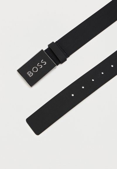 Ceinture synthétique noire avec une boucle en métal rectangulaire comportant le mot "BOSS" en lettres élégantes. La sangle possède plusieurs trous d'ajustement.