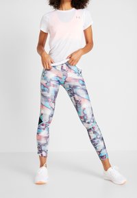 Valkoinen urheilupaita, jossa on hienovarainen gradientti ja logo, yhdistettynä värikkäisiin legginsseihin, joissa on abstrakti geometrinen kuvio pastelliväreissä ja mustissa yksityiskohdissa.