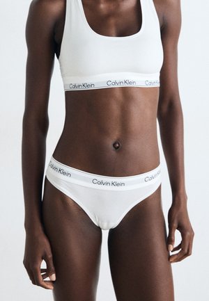 Witte katoenen bralette en bikini set met een zwart Calvin Klein logo band. Glad textuur, aansluitend ontwerp, minimalistische stijl.