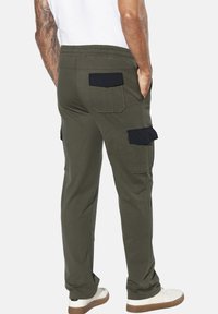 Grüne Cargo-Hosen aus Baumwollmischung mit schwarzen Akzenten und Taschen, elastischem Bund und lässiger Passform. Sichtbarer Knöchel- und Schuhdetail.