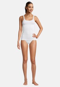 Top in cotone bianco con spalline decorate in pizzo, abbinato a lingerie bianca coordinata. Texture liscia, design semplice, che enfatizza il comfort.