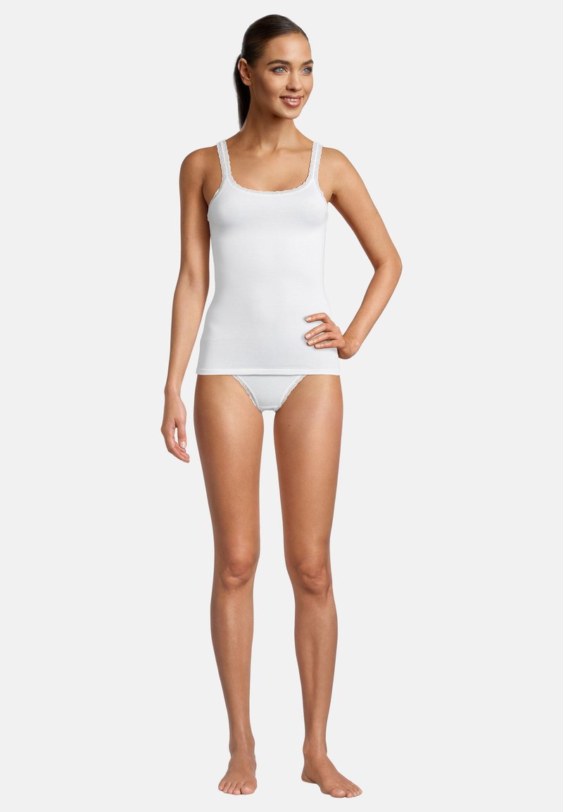Top in cotone bianco con spalline decorate in pizzo, abbinato a lingerie bianca coordinata. Texture liscia, design semplice, che enfatizza il comfort.