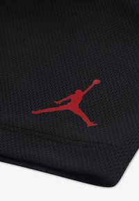 Melna tīkliņauduma audums ar teksturētu rakstu un izteiktu sarkanu Jumpman logotipu. Dizainā ir redzamas šuves gar malām.