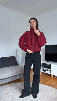 Rode cropped pufferjas met een ritssluiting aan de voorkant, gewatteerde textuur en hoge kraag, gecombineerd met zwarte wijde broekspijpen en zwarte schoenen.