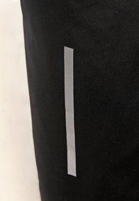 Černá sportovní tkanina má vertikální reflexní stříbrný pruh po jedné straně, což vytváří elegantní a funkční designový prvek.
