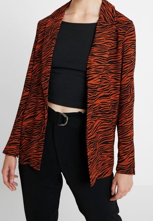 Czarno-czerwona marynarka w zebrę noszona na czarnym, krótkim topie i wysokich, czarnych spodniach z paskiem z srebrnym kółkiem.