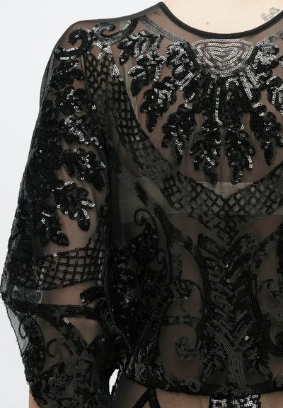 Fekete áttetsző szövet finom fekete flitteres hímzéssel, amely levél- és geometriai mintákat formál a ruhadarab felső részein és az ujjon.