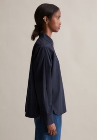 Marineblaues Langarmhemd mit einem Kragen zum Knöpfen, entspannter Passform und flachen, geknöpften Manschetten. Glatter Stoff mit dezentem Glanz.