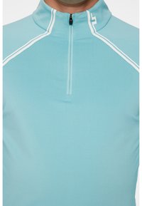 Ljusblå zip-up pullover med hög krage. Har vita accentlinjer längs axlarna och en fram-zip för att stänga. Slät tygtextur.