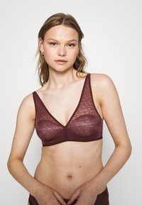 Burgundowy biustonosz typu bralette z teksturowaną, przezroczystą nakładką z delikatnym wzorem. Projekt w kształcie litery V oraz szerokie ramiączka zapewniają wygodne dopasowanie.