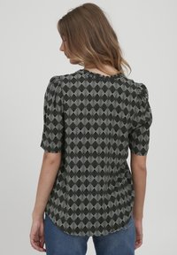 Blusa a maniche corte in bianco e nero con un motivo geometrico a ventaglio, scollatura tonda e dettagli plissettati sulle spalle. Vestibilità sartoriale.