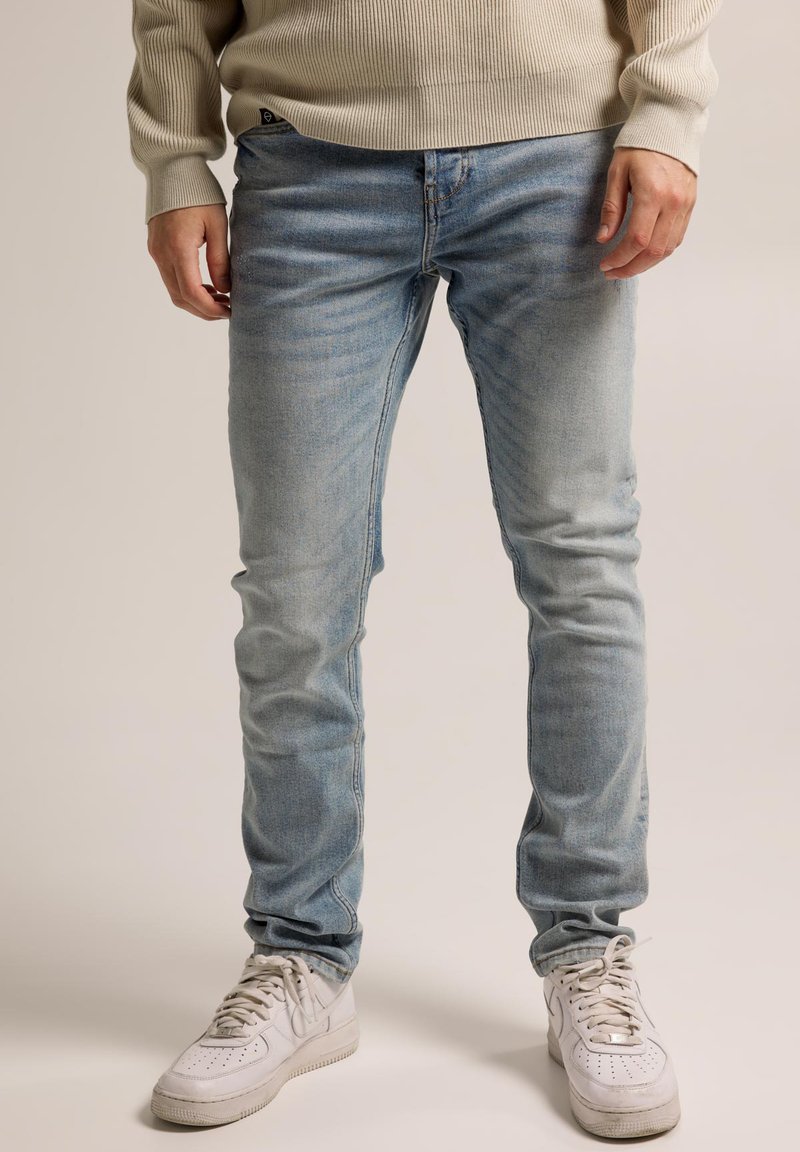 Light blue jeans made of denim, fitted design, with subtle fading and a classic five-pocket style, paired with white athletic shoes.