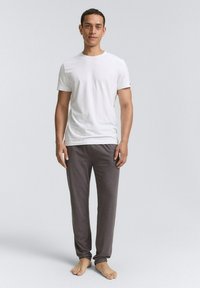 T-shirt blanc à col rond associé à un pantalon de lounge gris foncé. Le T-shirt est lisse, tandis que le pantalon a un tissu doux et légèrement texturé.