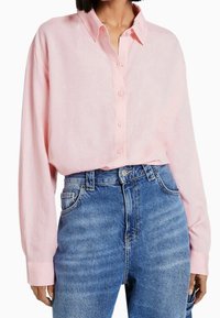 Light pink long-sleeve button-up shirt with a collared neck, paired with high-waisted blue denim jeans featuring front pockets.