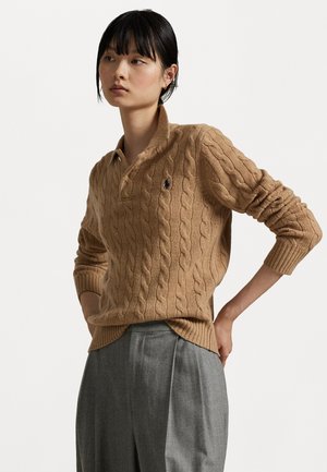Cable-knit, tan sweater with a collared neckline, ribbed cuffs, and hem; features a small logo on the chest. Paired with grey trousers.
