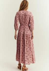 Maxi kjole i lys pink stof med blomsterprint, elastisk talje, puffede ærmer og flæsekant. Båret med brune klodsede hæle sandaler.