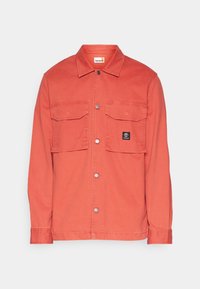 Mäns korallorange knapp-up jacka med två bröstfickor med lock, Timberland-logga på vänster ficka och en klassisk krage.