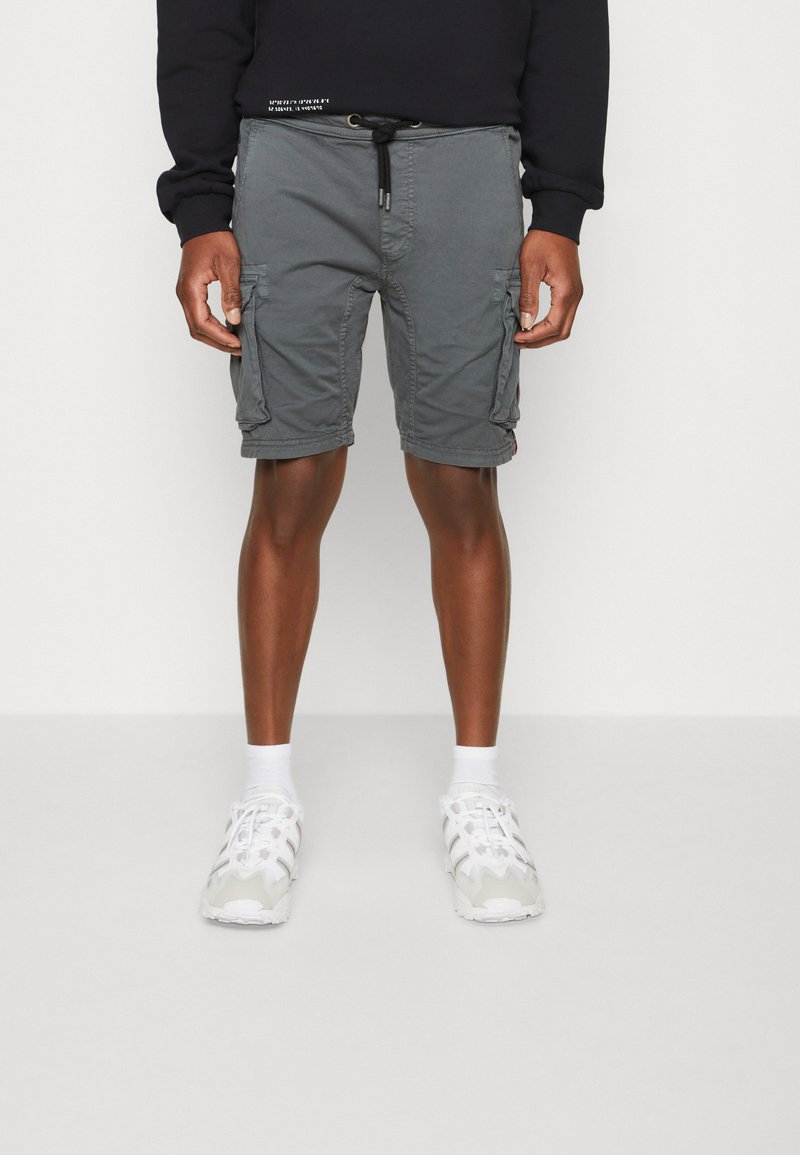 Grå cargo shorts med sidelommer, justerbar snor i livet og lett stoff. Brukt med hvite treningssko og sokker.
