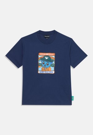 T-shirt bleu marine à manches courtes avec un graphisme d’un ours bleu portant une casquette verte et un gilet orange, étiqueté « Manga Bear Crew » et « Emporio Armani ».