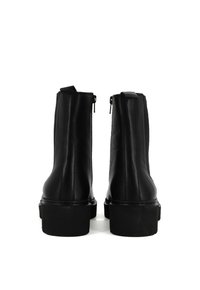 Stivali alla caviglia in pelle nera con una texture liscia, dotati di una suola chunky, cerniere posteriori e un design elegante e minimalista.