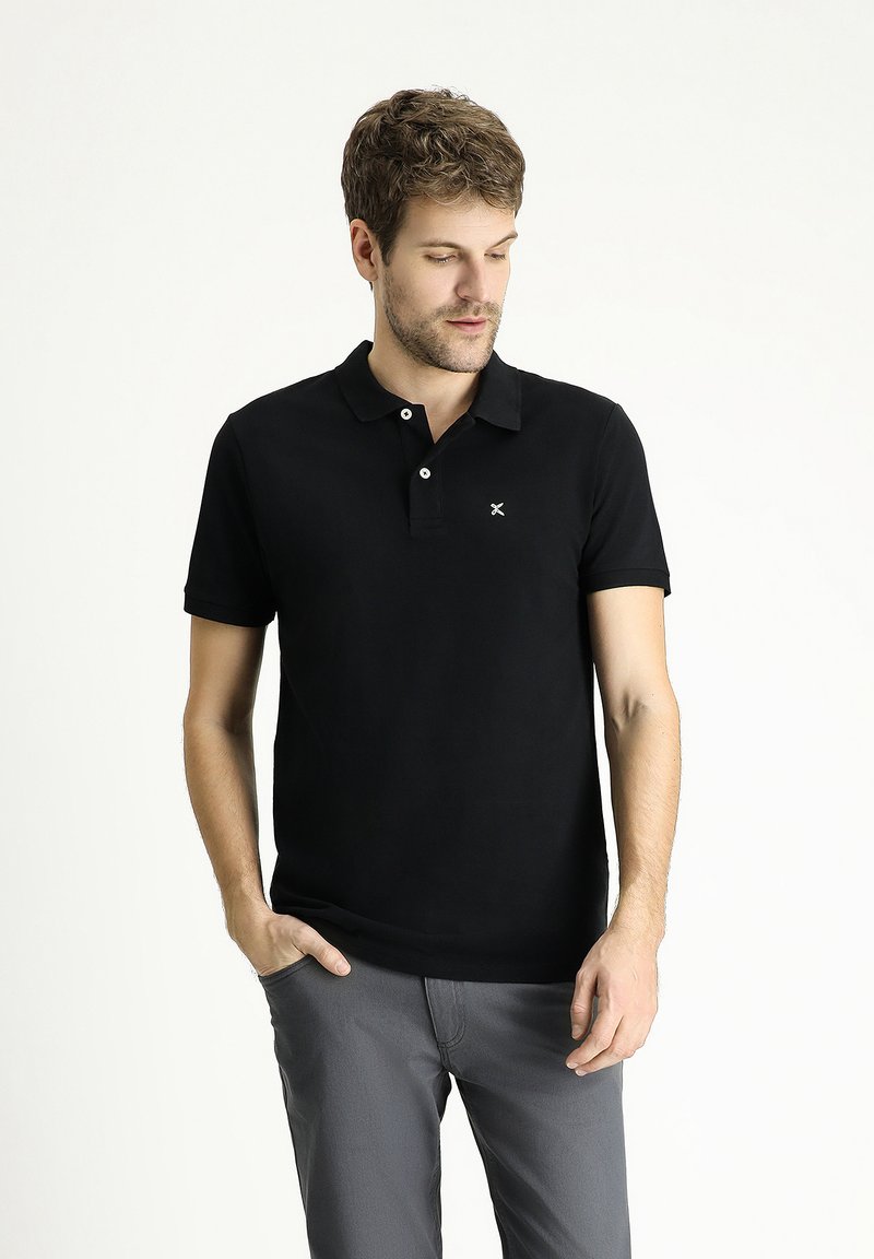 Polo negro con cuello clásico, dos botones frontales, mangas cortas y un pequeño logotipo blanco en el pecho; material de algodón suave.