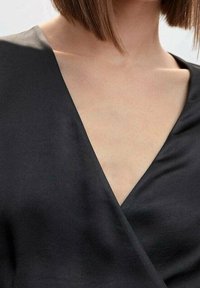Černý top s V výstřihem vyrobený z jemné látky a s draped designem. Výstřih je hluboký a zachycuje hladkou texturu, čímž vytváří elegantní vzhled.