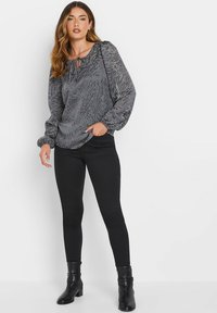 Blusa grigia con motivo e maniche a sbuffo, scollatura con fiocco, abbinata a leggings neri e stivali alla caviglia. Tessuto morbido e design aderente.