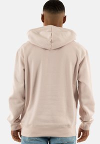 Felpa con cappuccio rosa chiaro, dal taglio rilassato, realizzata in un tessuto morbido, con polsini e orlo ribattuti. Presenta un design semplice e pulito, senza loghi visibili.