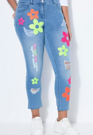 Lyseblå denimjeans med farverige blomsterlapper, slidte revner og sætningen "tvivl aldrig på dit potentiale" trykt på venstre ben.