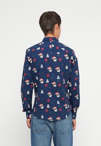 Camisa de color navy con patrones repetidos de caras de Santa, copos de nieve y árboles en rojo y verde. Mangas largas y cuello abotonado.